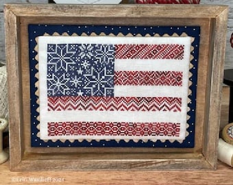 May include: A framed cross-stitch design of the American flag with a blue background and red and white stripes. The stitch count is 101 wide by 71 high. The artwork is designed by Erin Wasilieff.