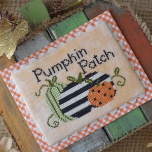 May include: A cross-stitch piece on a wooden pumpkin-shaped frame. The cross-stitch features a green, black and white striped, and orange pumpkin with the text "Pumpkin Patch".