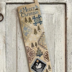 May include: A beige Christmas stocking with a white background and a variety of embroidered designs, including trees, snowflakes, and a swan. The stocking has the words "Merry Christmas" at the top and "Love Peace" at the bottom.
