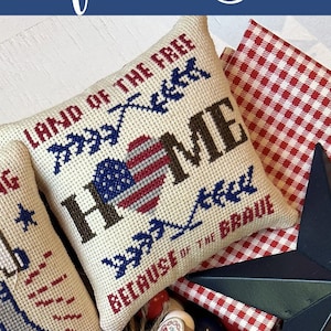 May include: A patriotic display featuring cross-stitched pillows with American flag and patriotic text, wooden beads, a star, and a wooden sign that says "Freedom". The arrangement is in a wooden tray.