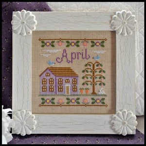 K&ouml;nnte beinhalten: Kreuzstich-Stickerei-Design mit einem lila Haus mit braunem Dach, einem Baum mit gr&uuml;nen Bl&auml;ttern und einem wei&szlig;en Kaninchen. Das Design ist in einem wei&szlig;en Rahmen mit floralen Akzenten gerahmt und das Wort "April" ist in der Mitte gestickt.