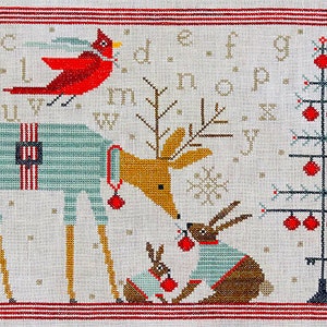 May include: Cross-stitch pattern featuring a reindeer wearing a blue and white striped sweater, a cardinal, a Christmas tree with red ornaments, and two bunnies wearing blue and white striped sweaters. The pattern includes the alphabet.