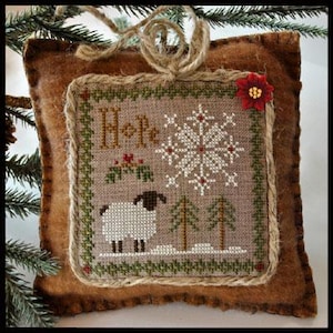 May include: A brown felt ornament with a stitched design of a white sheep, a snowflake, and the word "Hope". The ornament is decorated with a red flower.