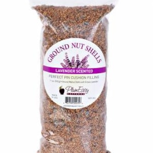 May include: A clear plastic bag filled with ground nut shells. The bag has a white top and a circular label with the text "GROUND NUT SHELLS" and "LAVENDER SCENTED". The label also reads "PERFECT PIN CUSHION FILLING".