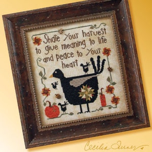 May include: A framed cross-stitch design featuring a black bird with a star-shaped design on its back. The bird is surrounded by pumpkins, leaves, and flowers. The text "Shale Your harvest to give meaning to life and peace to Your heart" is stitched in brown thread. The artist's signature "Cecilia Quner" is in the bottom right corner.