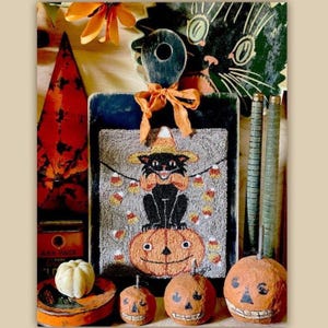 May include: A Halloween-themed arrangement featuring a decorative cutting board with a black cat on a pumpkin design, surrounded by carved pumpkins, a small gourd, and decorative elements in orange, black, and white.