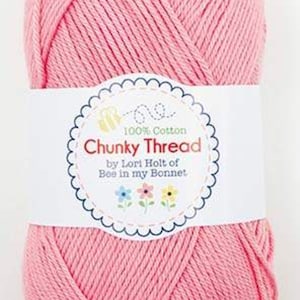 May include: A skein of pink chunky thread, 100% cotton, by Lori Holt of Bee in my Bonnet. The label is white with a scalloped edge and features the text "Chunky Thread" and floral illustrations.