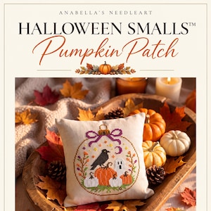 Op de afbeelding: Een vierkant kussen van gebroken witte stof met een kruissteekontwerp van een ronde kerstbal met een zwarte kraai, een wit spook en oranje pompoenen. De tekst Anabella's Needleart Halloween Smalls Pumpkin Patch staat erboven gedrukt.