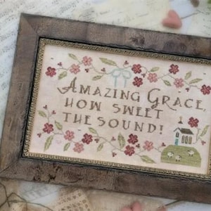 May include: Cross-stitch sampler in a rustic wooden frame. The text "AMAZING GRACE, HOW SWEET THE SOUND!" is surrounded by floral and leaf motifs. A small church and sheep are depicted at the bottom. The design is by Brenda Gervais.