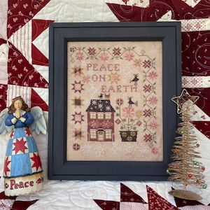 May include: A framed cross-stitch sampler with a red and white house, flowers, and birds. The text reads "Peace on Earth".