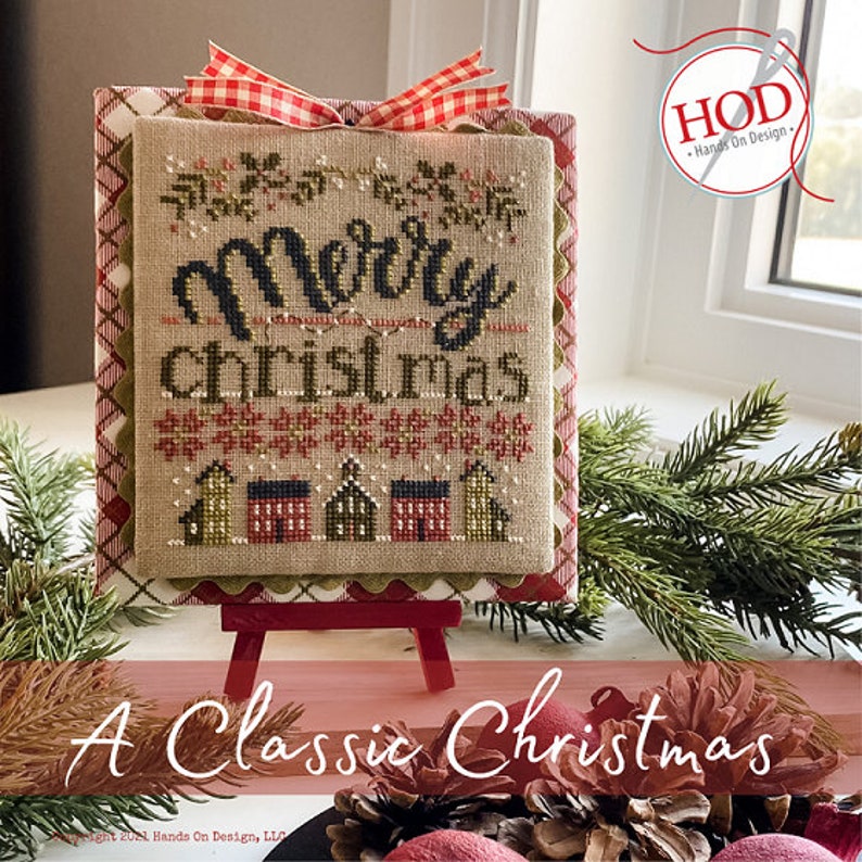 Pode incluir: Um sampler de ponto cruz com um la&ccedil;o de vichy vermelho e branco no topo. O sampler &eacute; emoldurado e apresenta o texto "Merry Christmas" com uma fonte estilizada e uma fileira de pequenas casas. O sampler est&aacute; em um cavalete de madeira e o texto "A Classic Christmas" est&aacute; abaixo do sampler.