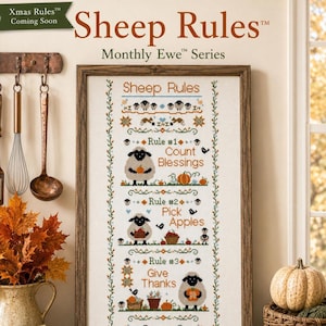 May include: A framed cross-stitch sampler titled Sheep Rules Monthly Ewe Series featuring three rules: Count Blessings, Pick Apples, and Give Thanks. The design includes illustrations of sheep, pumpkins, apples, and birds in orange, blue, and brown.