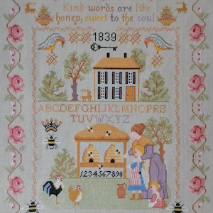 May include: A cross-stitch sampler with a yellow house, beehives, and a family of people. The text reads "Kind words are like honey, sweet to the soul 1839". The alphabet is also included, along with the numbers 1 through 9.