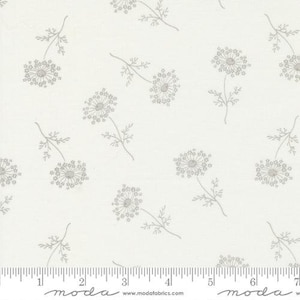 May include: White fabric with a repeating pattern of gray, stylized dandelion flowers. The fabric has a ruler with the word "moda" printed on it.