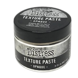 May include: A round jar of Ranger Distress Texture Paste Opaque with a black lid and black label. The label features white text reading Distress Texture Paste Opaque, 3 fl oz (88.7 ml), and descriptive text about the matte paste product.