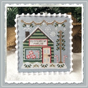 Puede incluir: Un patr&oacute;n de punto de cruz de una peque&ntilde;a casa de madera verde con un letrero que dice "Peppermint Parlor". La casa est&aacute; decorada con bastones de caramelo rojos y blancos y tiene una ventana con bastones de caramelo rojos y blancos en el interior. La casa est&aacute; rodeada de nieve y un peque&ntilde;o &aacute;rbol de hoja perenne.