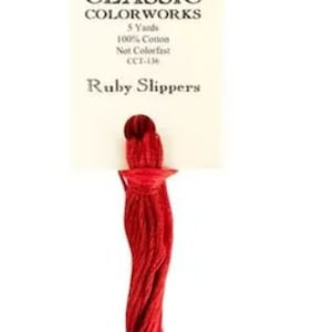May include: A skein of Classic Colorworks embroidery floss in a vibrant red color, labeled "Ruby Slippers." The label indicates it is 100% cotton, 5 yards in length, and not colorfast. Ideal for cross-stitch and embroidery projects.
