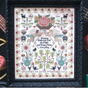 May include: A cross stitch pattern with a floral design and the text "I wanna Rock and Roll all Night and Cross Stitch every Day". The pattern is framed in a black frame and has a white background.