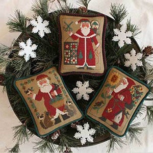 May include: Three embroidered Christmas pillow covers featuring Santa Claus in different scenes. The first pillow shows Santa with a sewing machine and a quilt, the second shows Santa with a basket of gifts and a bird, and the third shows Santa with a sunflower and a birdhouse.