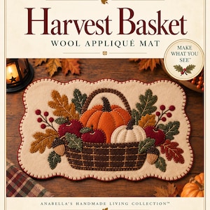 May include: A rectangular wool appliqué mat featuring a central brown basket filled with an orange pumpkin, a white pumpkin, red apples, acorns, and autumn leaves in shades of green, gold, and red. The mat has a scalloped edge with red stitching.