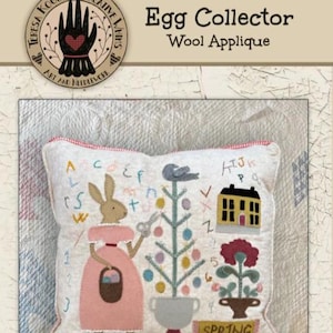 May include: A decorative pillow with a wool applique design featuring a bunny, a bird, a house, and a flower. The pillow has a red and white trim and the word "SPRING" is visible. The text "Egg Collector" and "Wool Applique" are also visible.