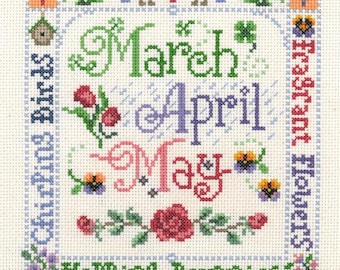 Op de afbeelding: Een kruissteekpatroon met het woord "Lente" in rood met bloemmotieven. De maanden maart, april en mei worden weergegeven in groen, paars en roze. Het patroon bevat ook afbeeldingen van vogels, bloemen en konijnen.