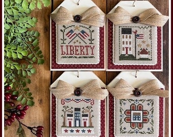 May include: Four framed cross-stitch patterns with a red, white, and blue theme. The patterns include a house, a flower, a flag, and the word "LIBERTY".