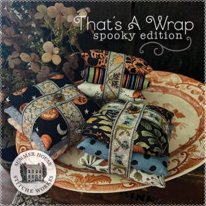 May include: Stacked fabric bundles with Halloween-themed patterns, including pumpkins and moons, are wrapped with decorative ribbon and a button closure. The text "That's A Wrap spooky edition" is visible.