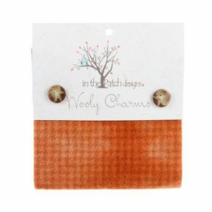 May include: A small piece of orange and brown patterned fabric with two brown buttons attached to a white card. The card has a tree illustration and the text "in the Patch designs" and "Wooly Charms".