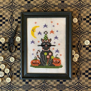 May include: Black cat wearing a party hat and a mustache, sitting on two orange pumpkins with jack-o'-lantern faces. The cat is surrounded by a crescent moon, stars, and purple flowers.
