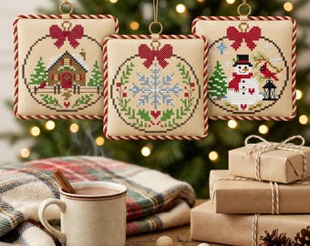 Può includere: Tre ornamenti quadrati a punto croce con disegni festivi: una baita, un fiocco di neve e un pupazzo di neve. Ogni ornamento presenta un bordo in corda intrecciata rossa e bianca, un fiocco rosso in alto e un gancio dorato.