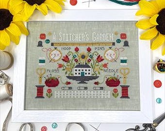 May include: A framed cross-stitch embroidery design titled "A Stitcher's Garden" featuring a house, flowers, and sewing supplies like a needle, thread, scissors, and a hoop.