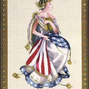 May include: Cross-stitch artwork of a woman in a draped gown holding a flag with red and white stripes and a blue field of stars. She wears a laurel wreath and is framed in a gold-colored ornate border.