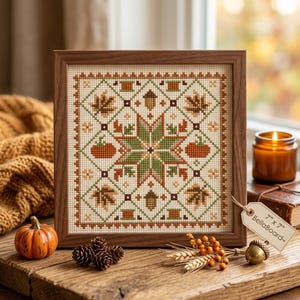 Könnte beinhalten: Eine quadratische Kreuzstichstickerei in einem braunen Holzrahmen mit einem zentralen Sternmuster, umgeben von herbstlichen Motiven wie orangefarbenen Kürbissen, braunen Eicheln und Ahornblättern. Ein Etikett am Rahmen zeigt 7" x 7" BellaBoard.