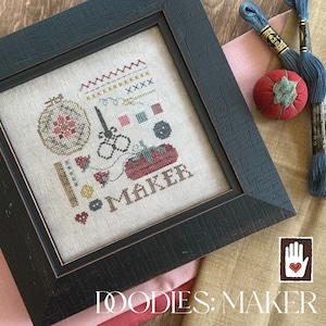 May include: A framed cross-stitch design with a light brown background and the word "MAKER" in red lettering. The design includes a variety of sewing-related items, such as a spool of thread, scissors, and a thimble. The frame is black and has a distressed finish.