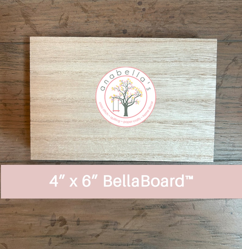 May include: A 4 inch by 6 inch wooden board with a light brown wood grain finish. The board has a sticker on it that says "Anabella's" with a tree and swing design. The sticker also says "cross stitch - quilting - paper crafts - home decor". The board is labeled "4" x 6" Bella Board&trade;".