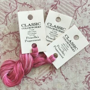 May include: Three skeins of embroidery floss in the color "Priscilla's Peppermint". The floss is a gradient of pink and white. The skeins are labeled "Classic Colorworks" and "100% Cotton".