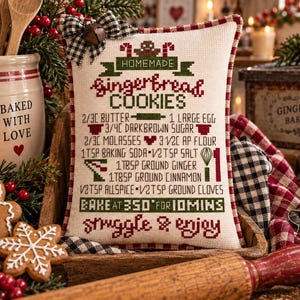 May include: A rectangular decorative pillow featuring cross-stitched text and graphics for a gingerbread cookie recipe. The design includes a black and white buffalo check bow, red and green accents, and the text "HOMEMADE GINGERBREAD COOKIES" with a list of ingredients and baking instructions.