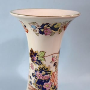 May include: A white ceramic vase with a gold rim and a floral pattern in shades of blue, pink, and green.