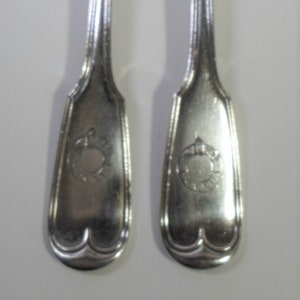 May include: Two silver forks with four tines each, displayed against a white background. The handles have a decorative design and a crest. The forks are likely for formal dining.