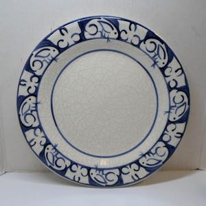 May include: A round ceramic plate featuring a white center with a fine crackle glaze finish. The wide rim is decorated with a repeating pattern of stylized blue rabbits in a circular arrangement against a white background, creating a border.