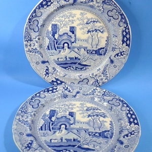 May include: Two blue and white porcelain plates with a scenic design of a bridge and trees. The plates have a scalloped edge and a floral pattern.