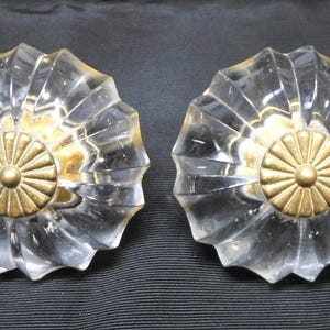 以下が含まれることがあります： 星型のデザインと金色の金属製センターを備えた、2つの透明なガラス製キャビネットノブ。ノブはファセット加工されたスカラップエッジで、家具や装飾用である可能性があります。
