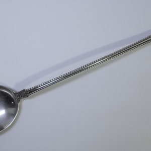 May include: A silver serving spoon with a long, ornate handle and a rounded bowl. The handle is decorated with a beaded pattern.