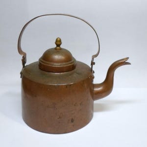 May include: A copper kettle with a rounded body, a curved spout, and a hinged handle. The lid is topped with a small, decorative finial. The kettle has a vintage appearance and is likely used for boiling water.