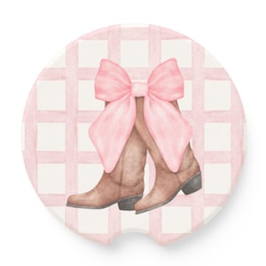 May include: A pink and white gingham patterned coaster with a pair of brown cowboy boots tied together with a large pink bow.