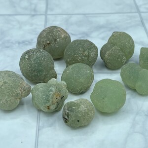 Peut inclure: Une collection de dix pierres rondes et de forme irrégulière, translucides et vertes. Les pierres ont une surface rugueuse et texturée.