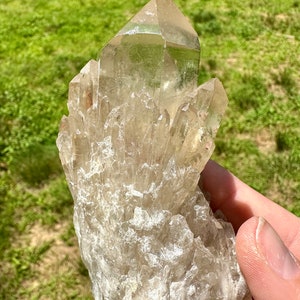 May include: A large, clear quartz crystal cluster with a pointed, faceted top. The crystal is surrounded by smaller, clear quartz crystals.