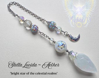 Puede incluir: Un adorno para coche de temática celestial con una cadena plateada, cuentas iridiscentes y un colgante de cristal. El adorno presenta el texto "Stella Lucida - Aether" y la frase "bright star of the celestial realms."