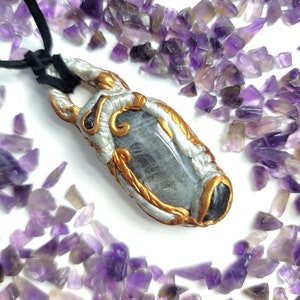 May include: A silver and gold pendant with a clear stone set in a decorative frame. The pendant is surrounded by small purple amethyst crystals.
